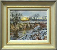 Load image into Gallery viewer, A bend in the River Welland at Duddington, with snow on the foreground bank and a fierce sun breaking on the skyline of distant trees, and a Hawthorn bush on the far riverbank on the left. Photo shows the frame with an off-white inner slip, a gold ribbed line then a gradated frame with a buff inner edge and a grey outer edge.
