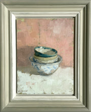 Load image into Gallery viewer, 9.5 x 7 inch oil on linen board, with four round dishes stacked together, sitting on a white cloth with a pinkish/red backdrop. Painted with loose brushstrokes with much of the ochrey underpainting showing through. Shows the hand-painted frame, coloured off-white inner edge to greenish/grey outer edge, the painting &#39;floating&#39; with a small space all around.
