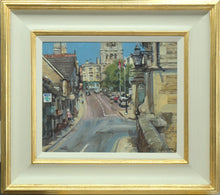 Load image into Gallery viewer, 10 x 12 inch oil painting, painted from the town bridge, with the bridge wall in the right foreground, part of a stone building on right, looking up the hill with shops in shadow on the left, and the sunlit church at the top centre, against a clear, blue sky. Also shows the scooped ivory coloured frame with gold outer and inner edges, and off-white slip.
